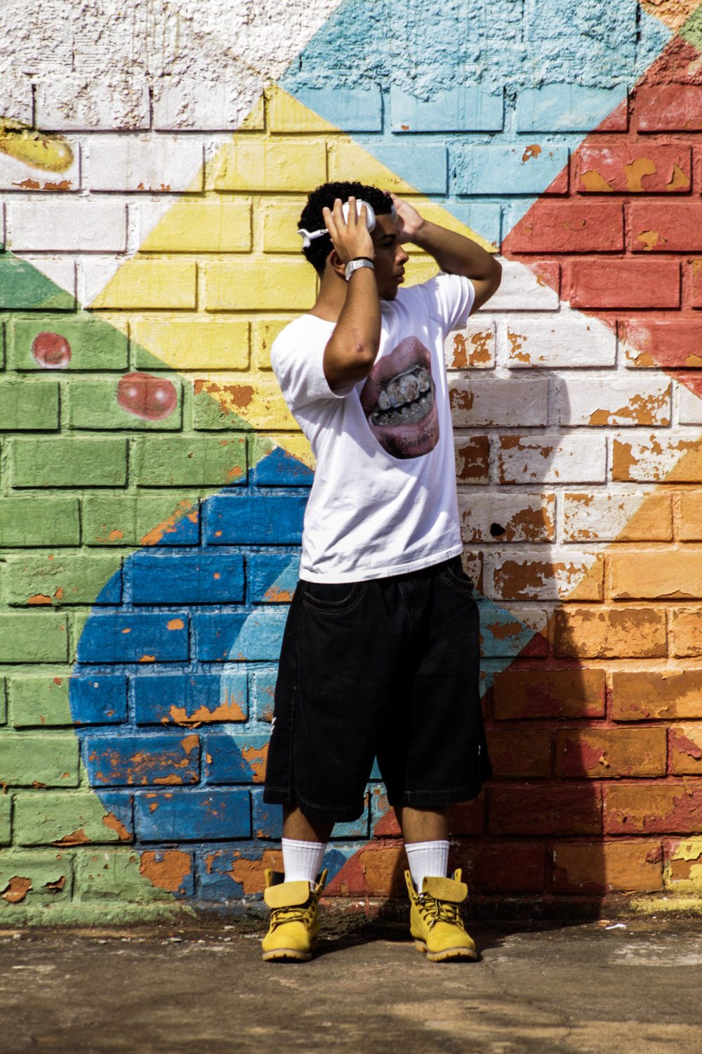 Feliphe de pé diante do muro colorido, mãos na cabeça